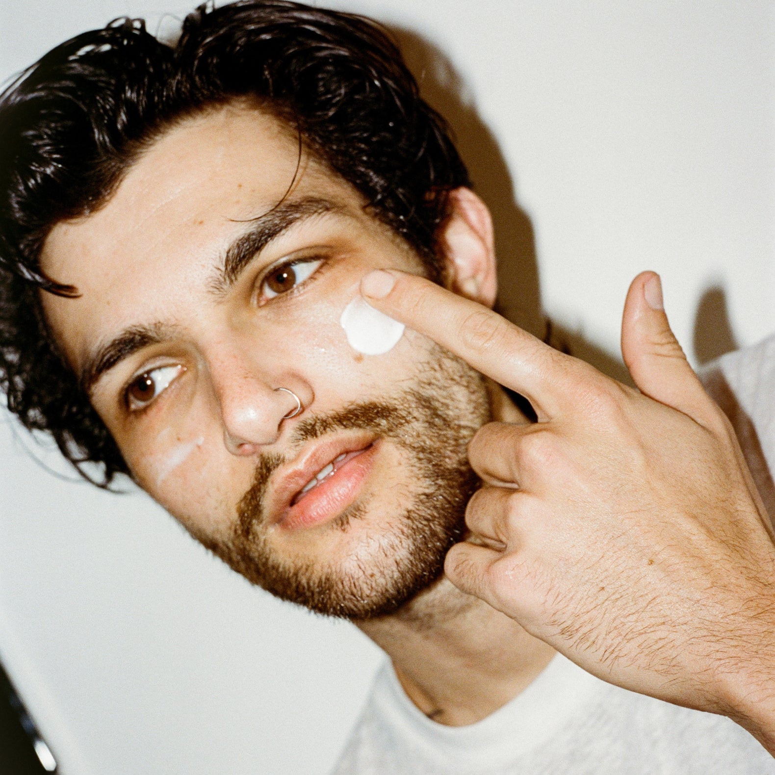 Man applying 'COMUNE' Hydra Shroom cream to his face with a neutral background