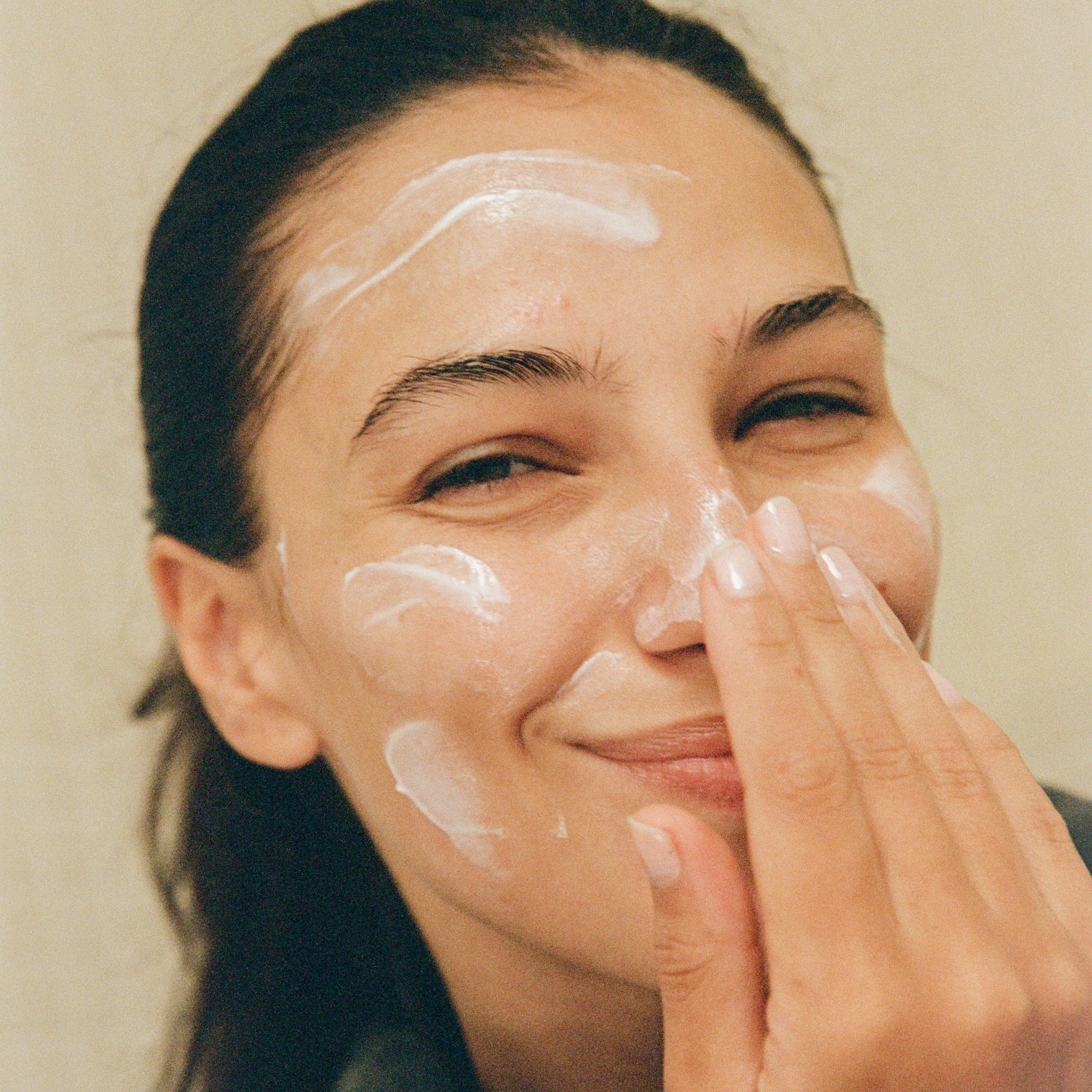 Woman applying 'COMUNE" Hydra Shroom Cream to her face with a neutral background