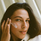 Woman applying 'COMUNE' Revitalize Overnight Mask dual night cream to her face with a neutral background.