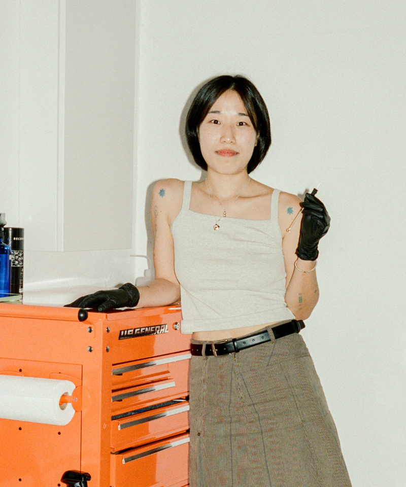 COMUNE artist Odni Lim wearing a white tank top and gloves in front of an orange toolbox.