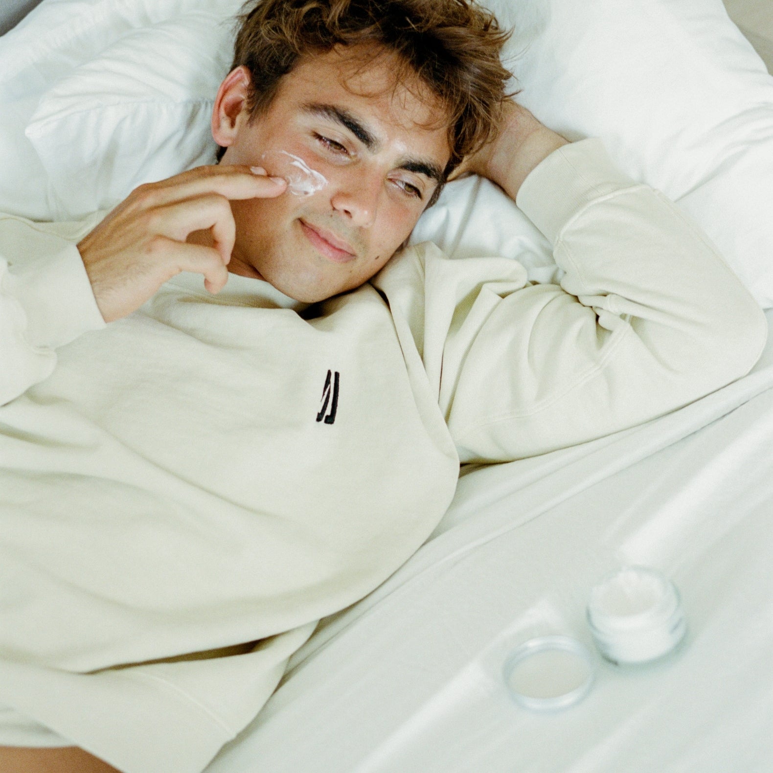 Man applying COMUNE Revitalize Overnight Mask to his face in bed.  