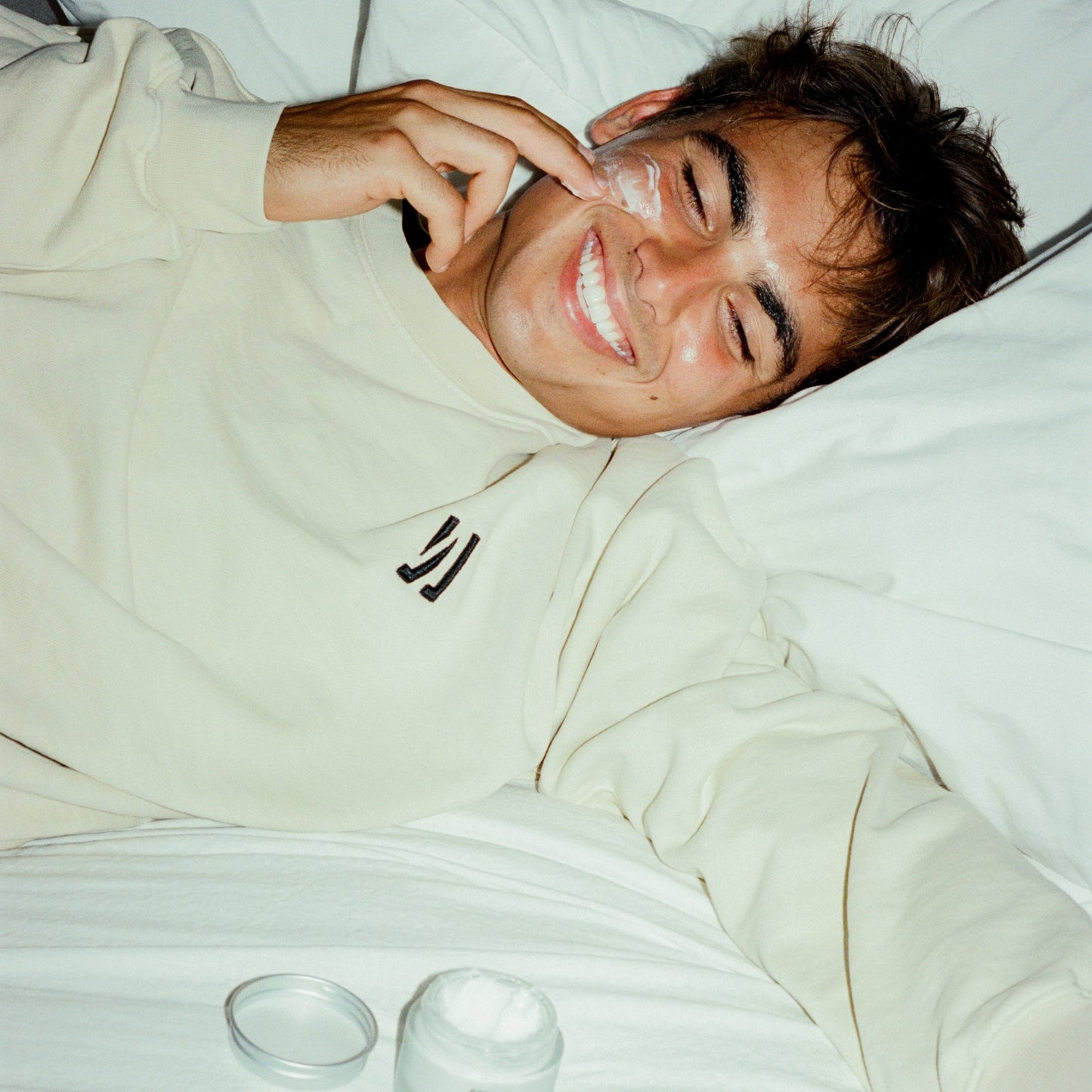 Person lying on a bed applying and with COMUNE Revitalize Overnight Mask product nearby