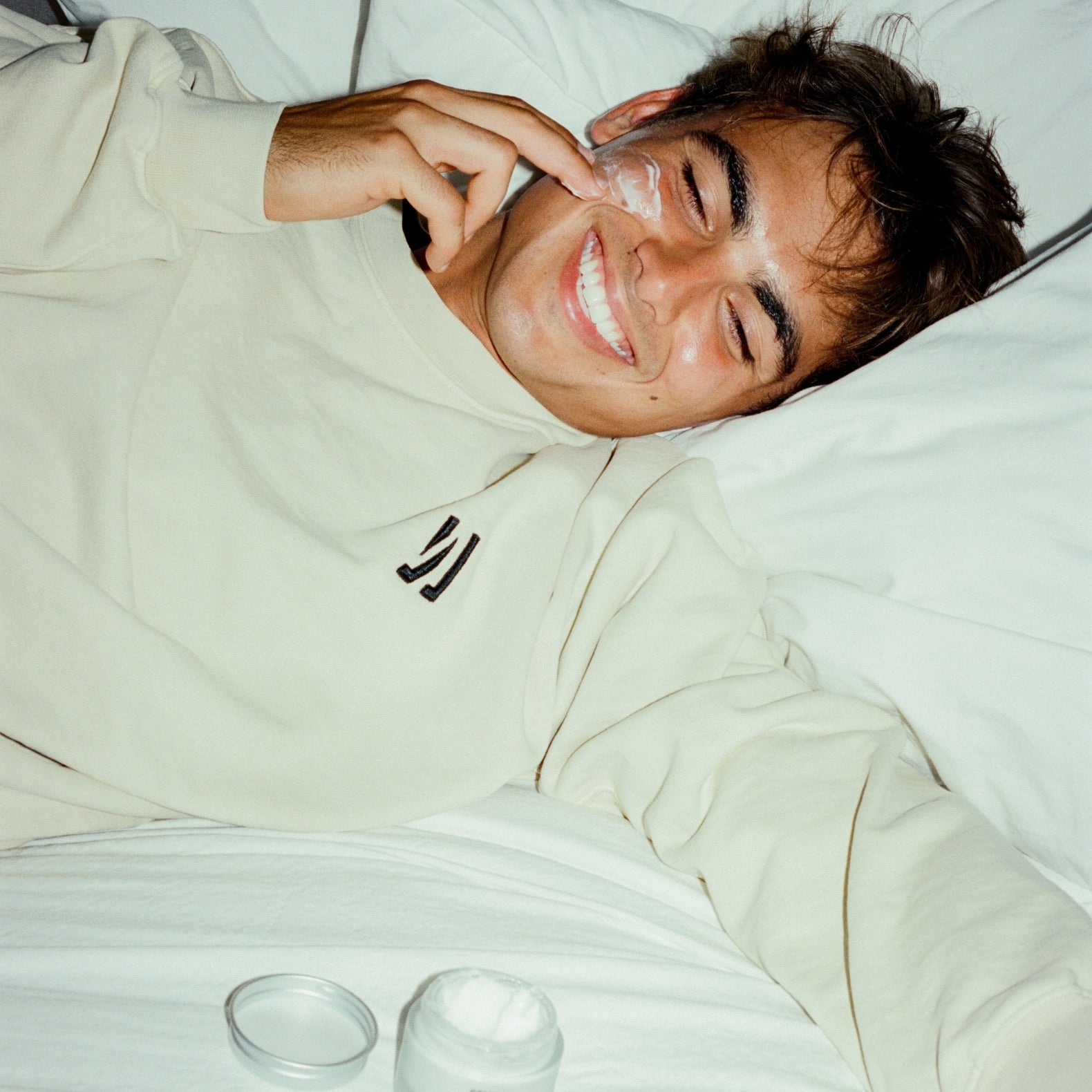 Person lying on a bed applying and with COMUNE Revitalize Overnight Mask product nearby