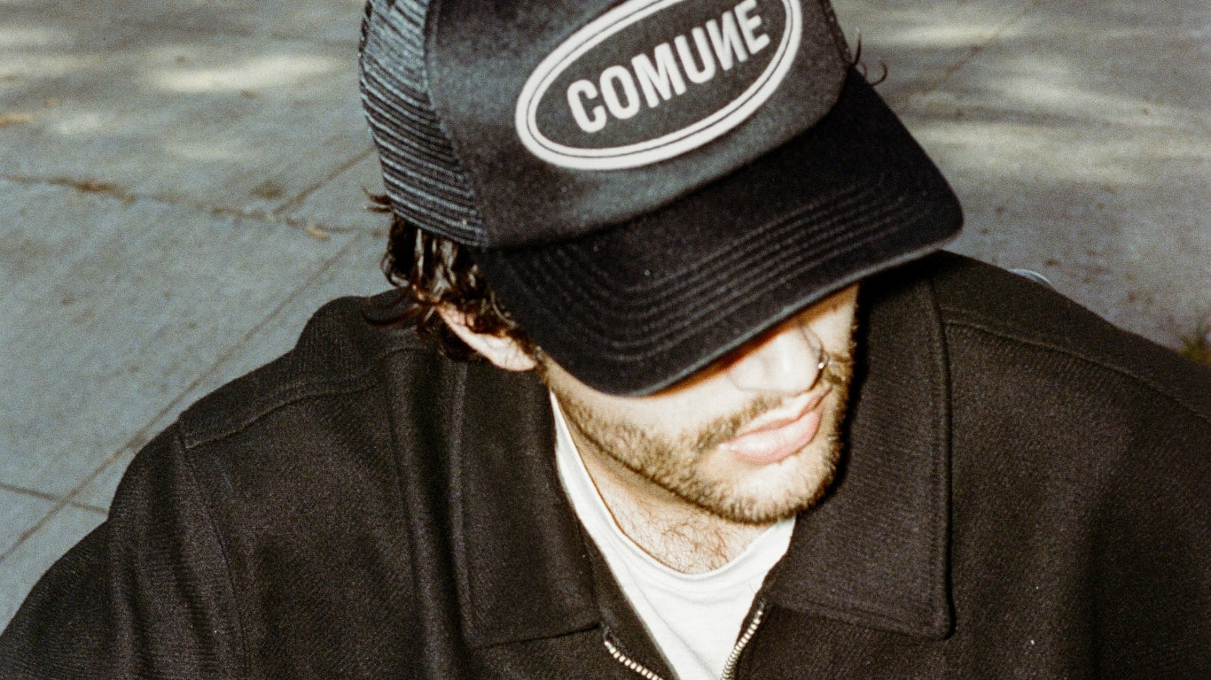 Person wearing a black cap with 'COMUNE' logo and dark jacket.