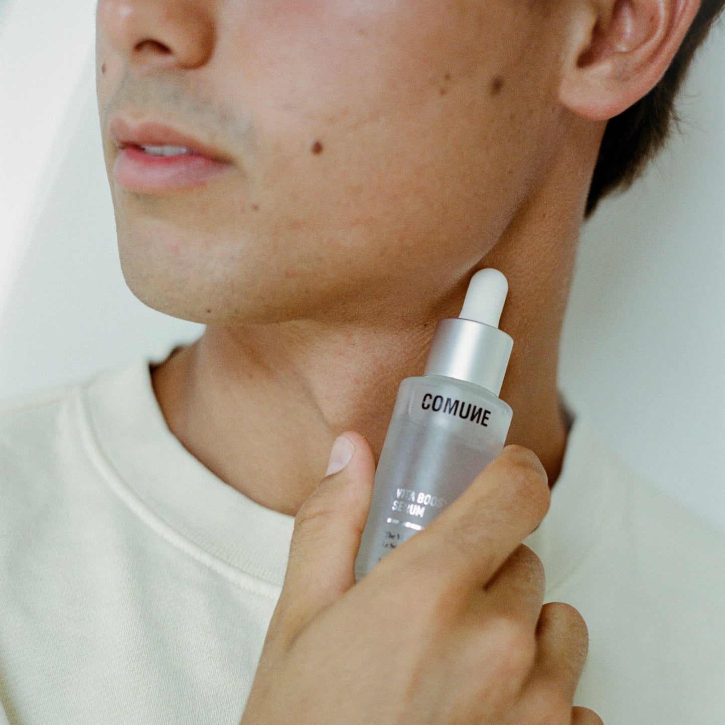 Person holding COMUNE Vita Boost Serum next to his face