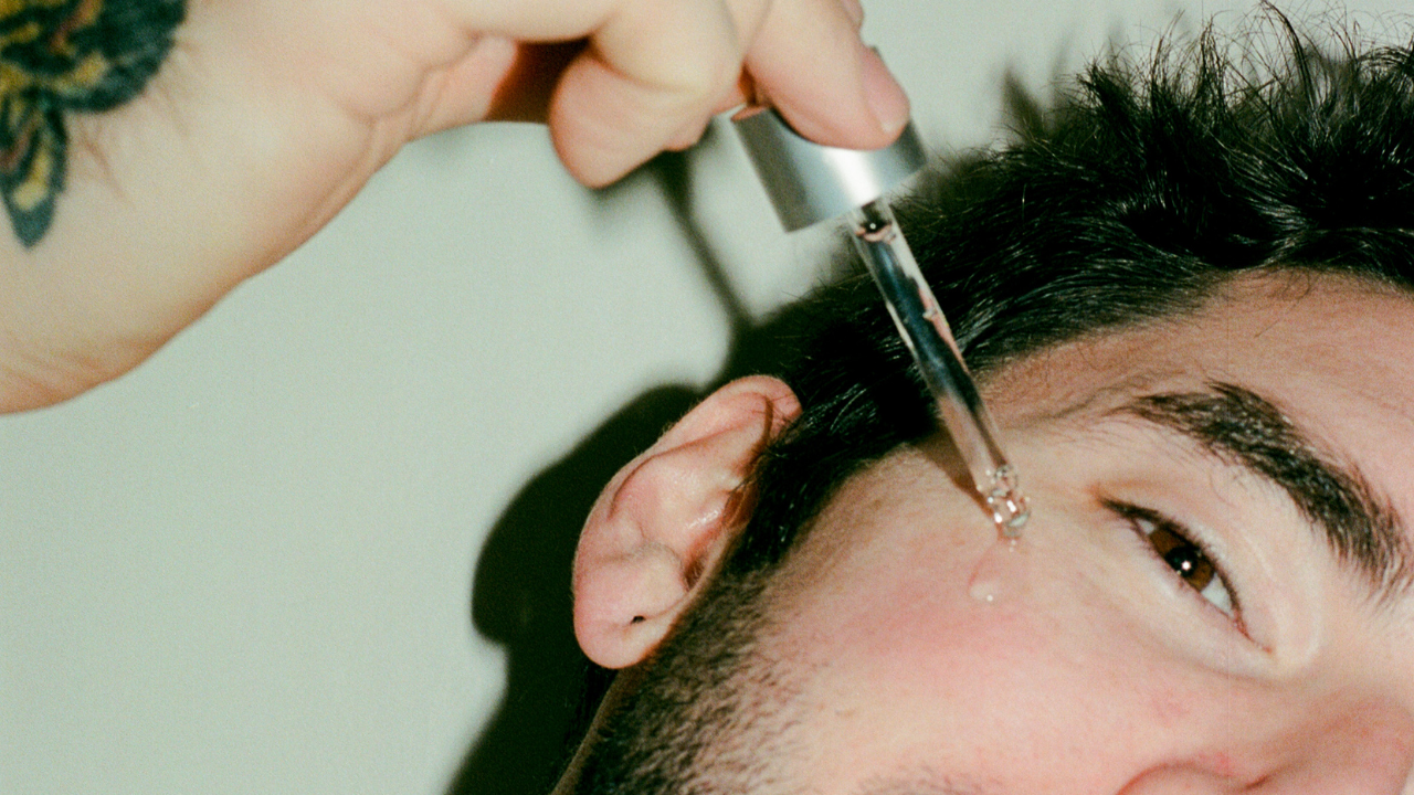 COMUNE artist Ethan applying a dropper of comune Vita Boost Serum on his face.