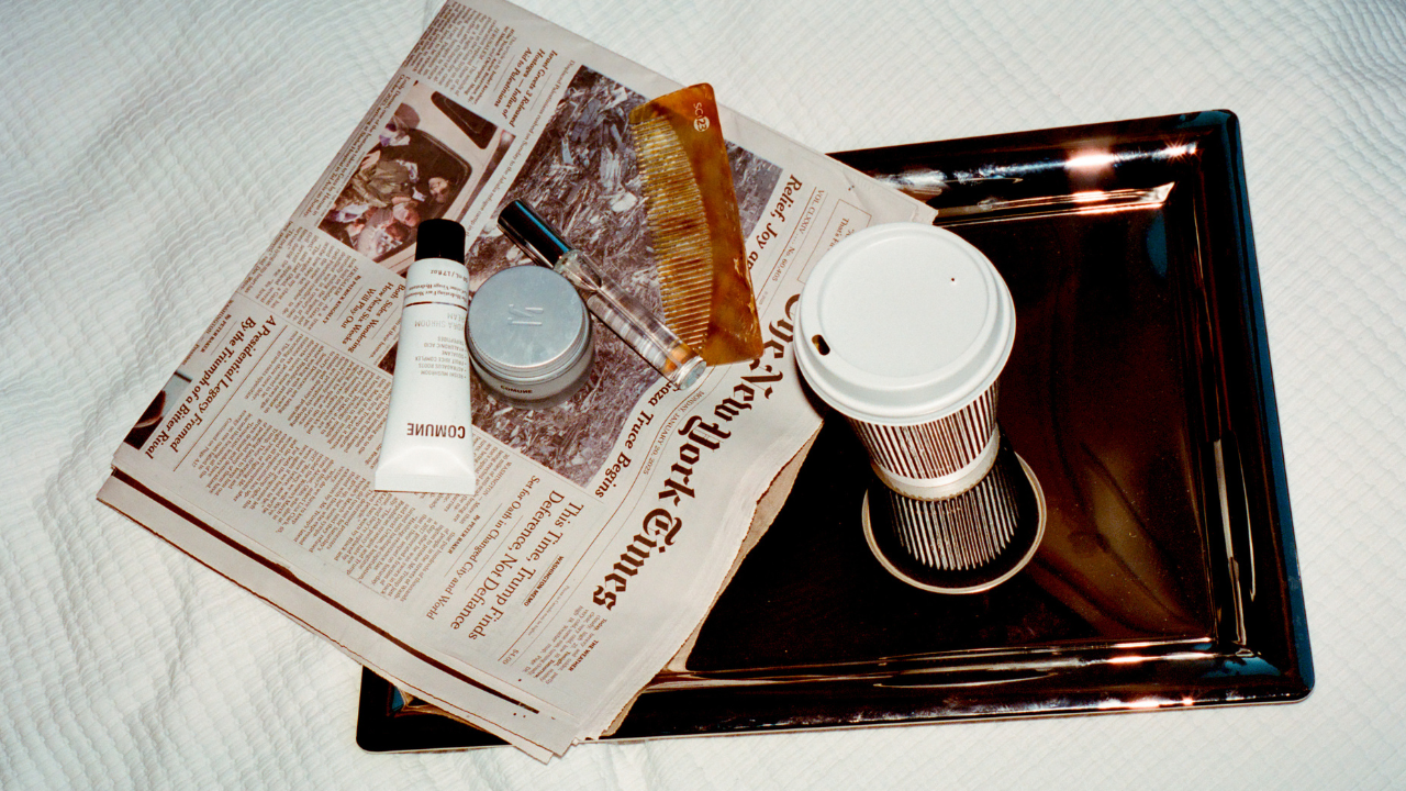 Newspaper with 'COMUNE' skincare products and a coffee cup on a tray